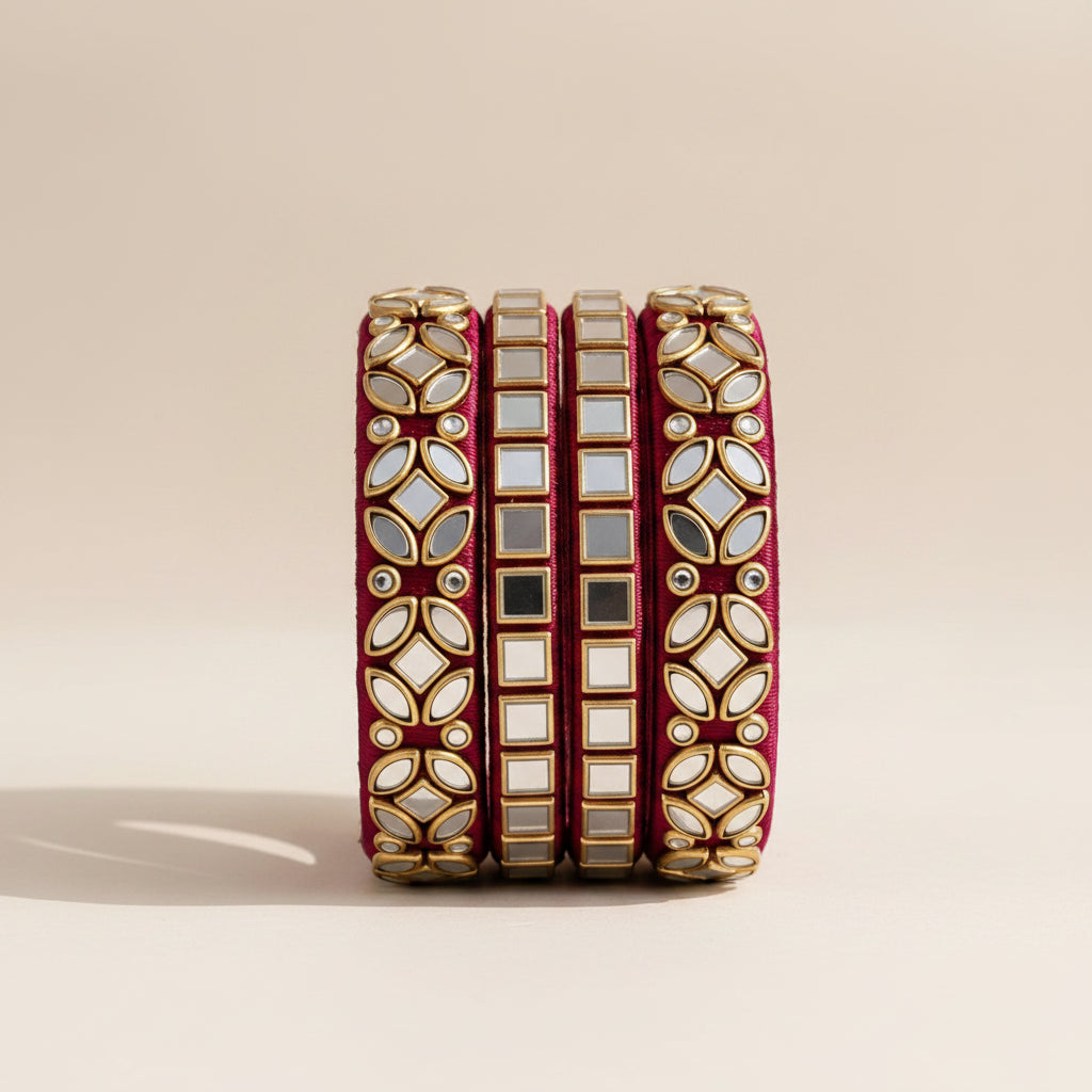 A set of five traditional Indian bindi bracelets stacked on a white pedestal. The bracelets feature a deep red velvet inner lining and a gold-plated outer band decorated with white and clear mirror work, red floral accents, and gold borders.
