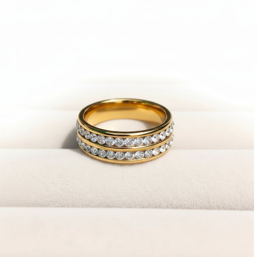 Two gold rings with rows of clear pavé stones, displayed on a soft cream-colored surface against a white background.