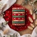 A stack of traditional Indian bangles with red, green, and gold embroidery and sequins, displayed on a red fabric cloth with decorative dried flowers and eucalyptus leaves.