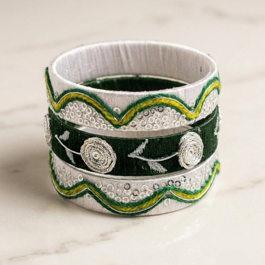 A stack of three wide bangles with dark green velvet bands, silver-toned textured borders, and green and yellow embroidered scalloped edges, displayed on a light marble surface.