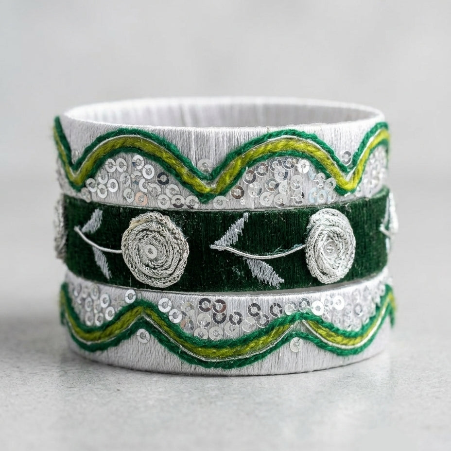 A wide silver-toned band bracelet decorated with dark green velvet bands, green and yellow embroidered scalloped edges, sequins, and raised floral rosettes, shown on a light gray background.