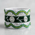 A wide silver-toned band bracelet decorated with dark green velvet bands, green and yellow embroidered scalloped edges, sequins, and raised floral rosettes, shown on a light gray background.