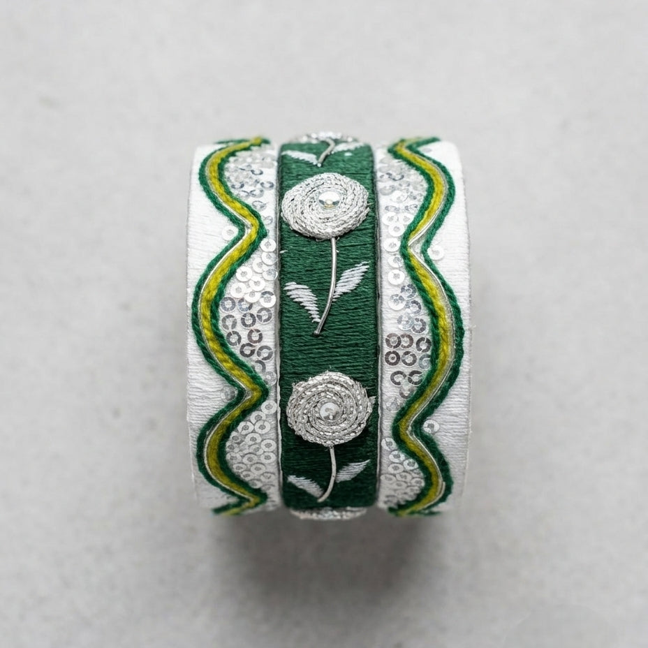 A handmade ring featuring three vertical bands: a central dark green band with silver floral embroidery, flanked by two white bands with green and yellow wavy patterns and silver dots.