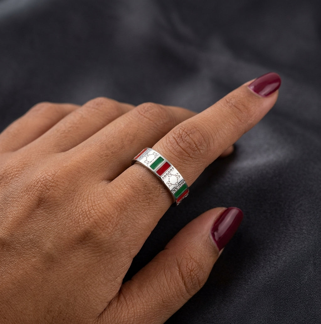 A close-up of a hand wearing a silver ring with a central rectangular inlay featuring green, white, and red stripes, set against a dark textured background.
