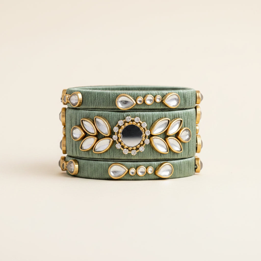 A green velvet clutch bag with gold-plated hardware and white stone embellishments, styled flat-lay on a burlap background with dried grass and green leaves.