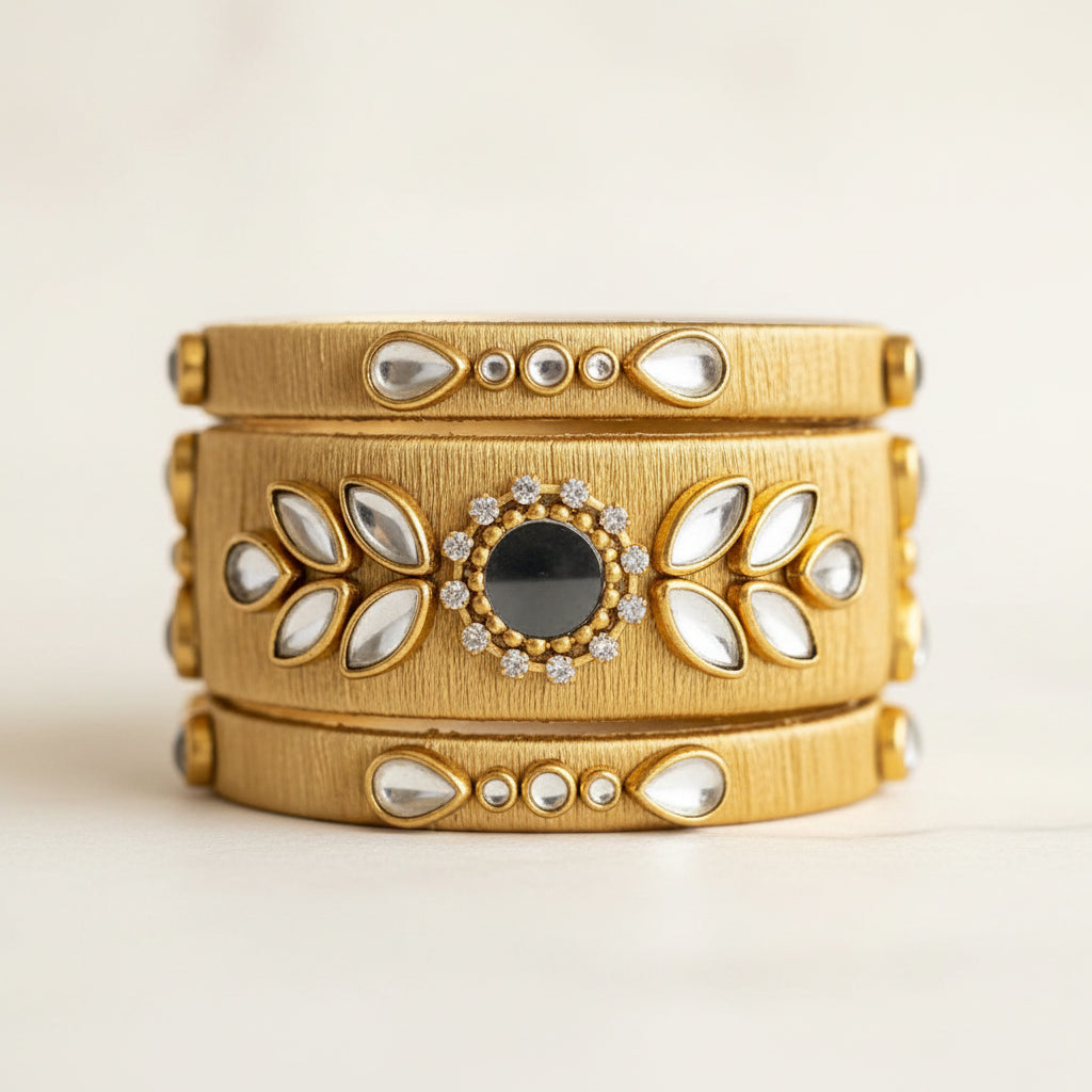 A wide gold-toned multi-band cuff bracelet with inlaid white stones and a central dark stone, photographed on a light marble surface with warm string lights blurred in the background.