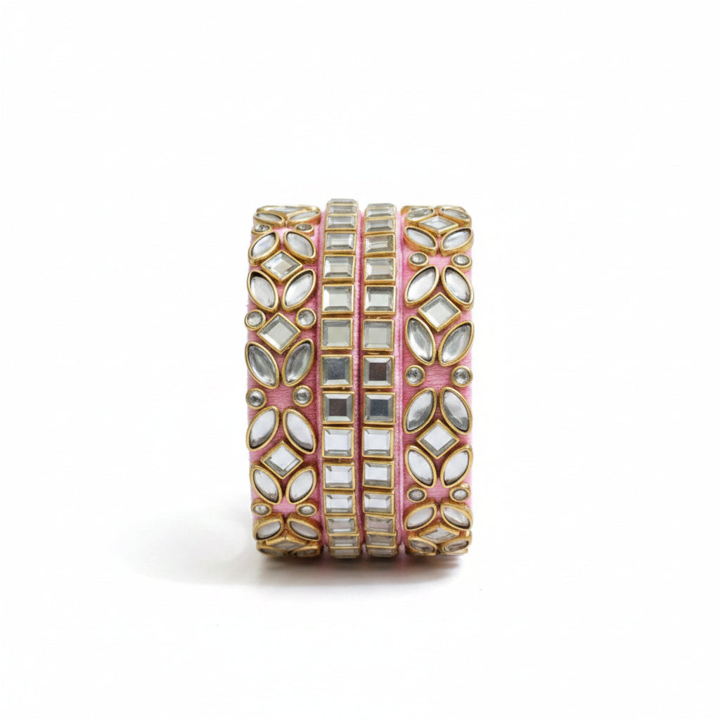 A pink velvet cuff bracelet adorned with gold-plated metal and clear mirror work, styled on a soft pink and beige fabric background with eucalyptus sprigs.