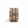 A wide gold-toned bangle bracelet decorated with multiple rows of white stones and a deep red velvet interior, styled on a white marble surface with draped white fabric and gold leaf accents.