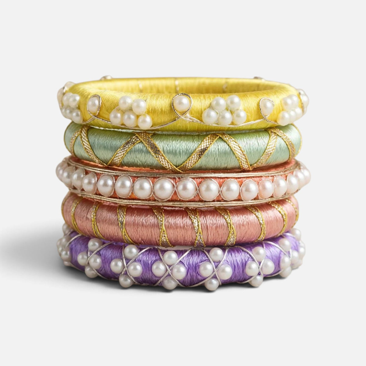 A stack of five traditional Indian Kundan bangles in yellow, mint green, rose gold, pink, and purple, each adorned with white pearls and gold embroidery, set against a clean white background.