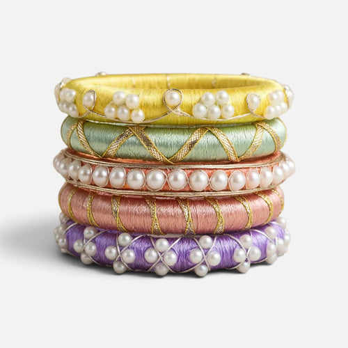 A stack of five traditional Indian Kundan bangles in yellow, mint green, rose gold, pink, and purple, each adorned with white pearls and gold embroidery, set against a clean white background.