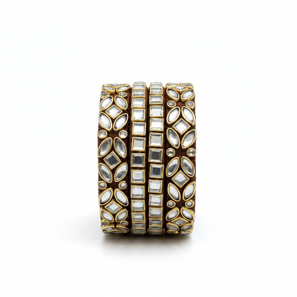 A wide gold-toned cuff bracelet with multiple rows of clear rhinestones and mirrored stones, styled on a burlap surface with cream fabric, eucalyptus branches, and small white flowers.