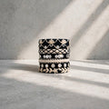 A stack of four black and white patterned bangles with intricate floral and geometric designs, styled on a textured light gray surface under soft diagonal sunlight.