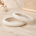 Sitara white pearl beaded handcrafted bangles held in a hand against a lush green outdoor background