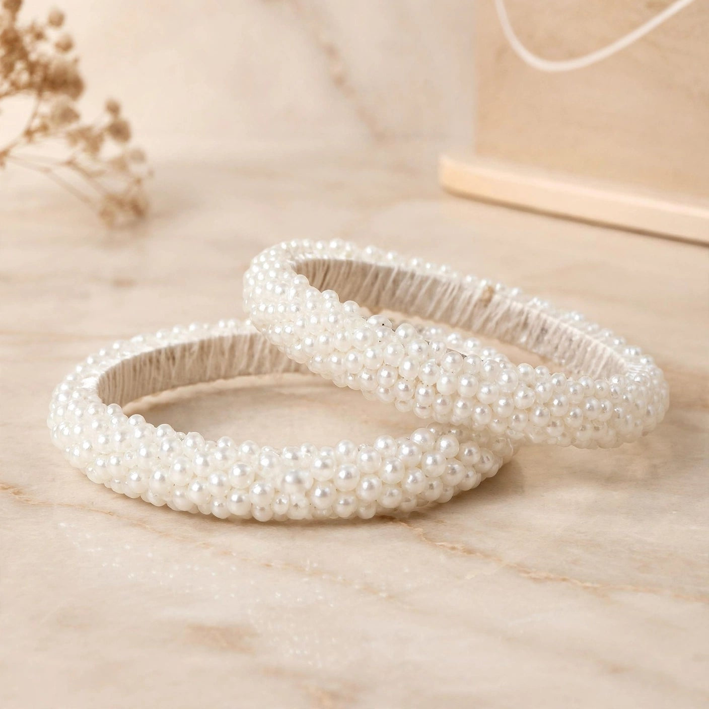 Sitara white pearl beaded handcrafted bangles held in a hand against a lush green outdoor background