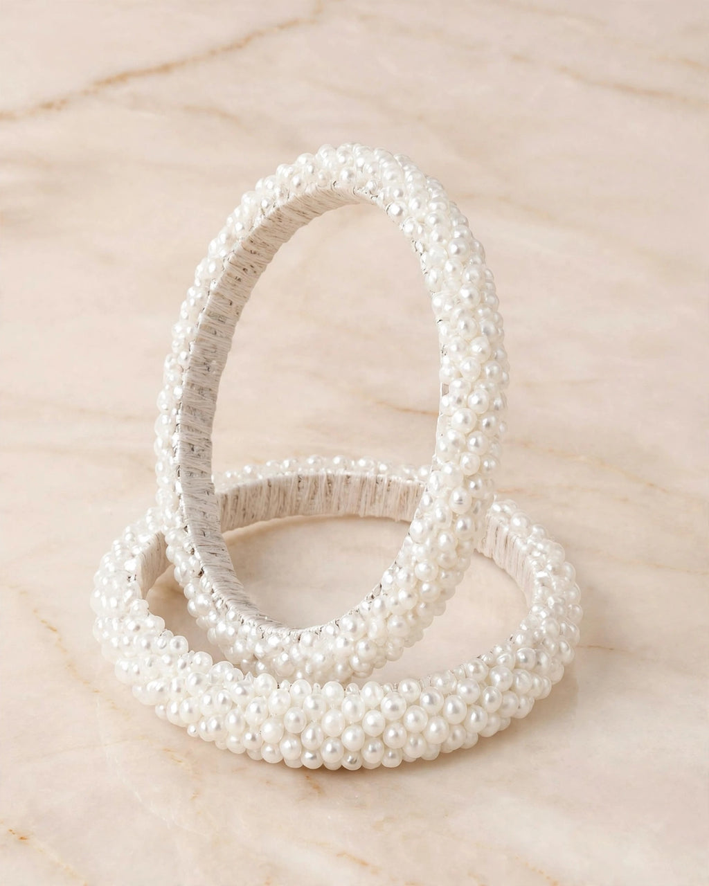 Sitara white pearl beaded handcrafted bangles held in a hand against a lush green outdoor background