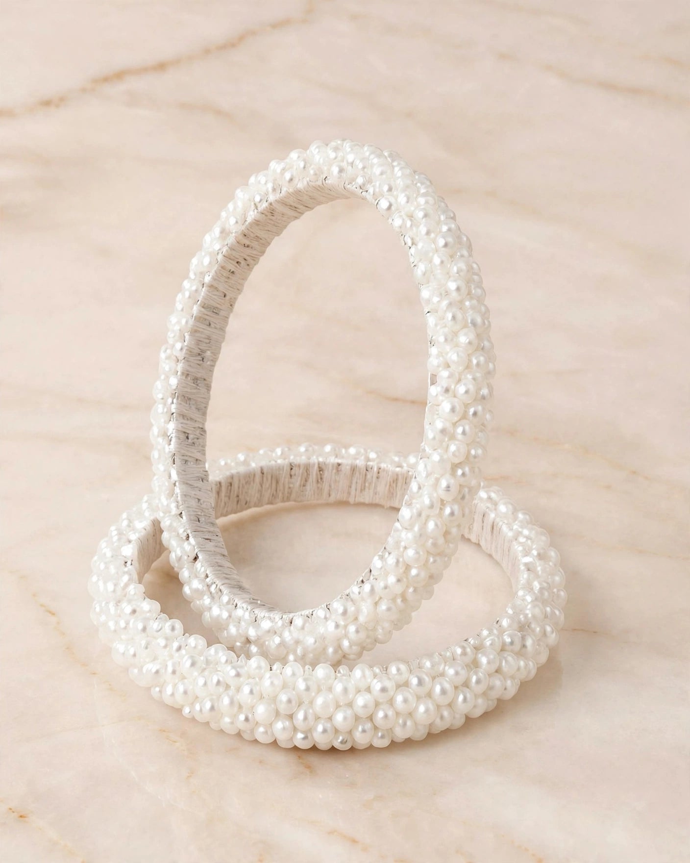 Sitara white pearl beaded handcrafted bangles held in a hand against a lush green outdoor background