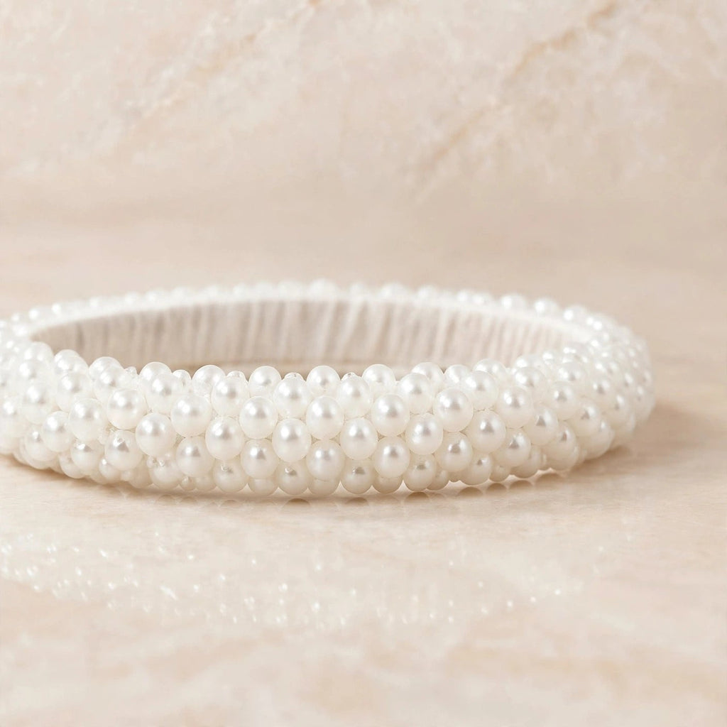 Sitara white pearl beaded handcrafted bangles held in a hand against a lush green outdoor background